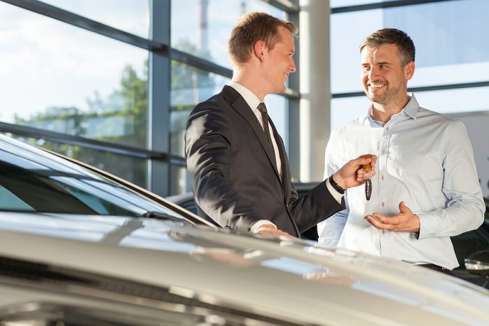 Photo of car dealer selling car to happy buyer