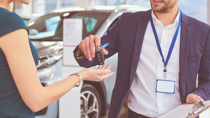 Car salesman sells a car to happy customer in car dealership and hands over the keys