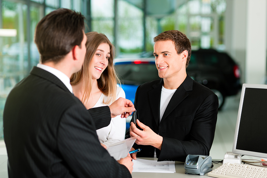 Sales situation in a car dealership, the young couple gives the key of a sold car