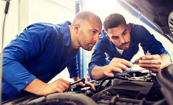 auto service, repair, maintenance and people concept - mechanic men with wrench repairing car at workshop