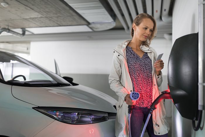 Young woman charging an electric vehicle in an underground garage equiped with e-car charger. Car sharing concept.